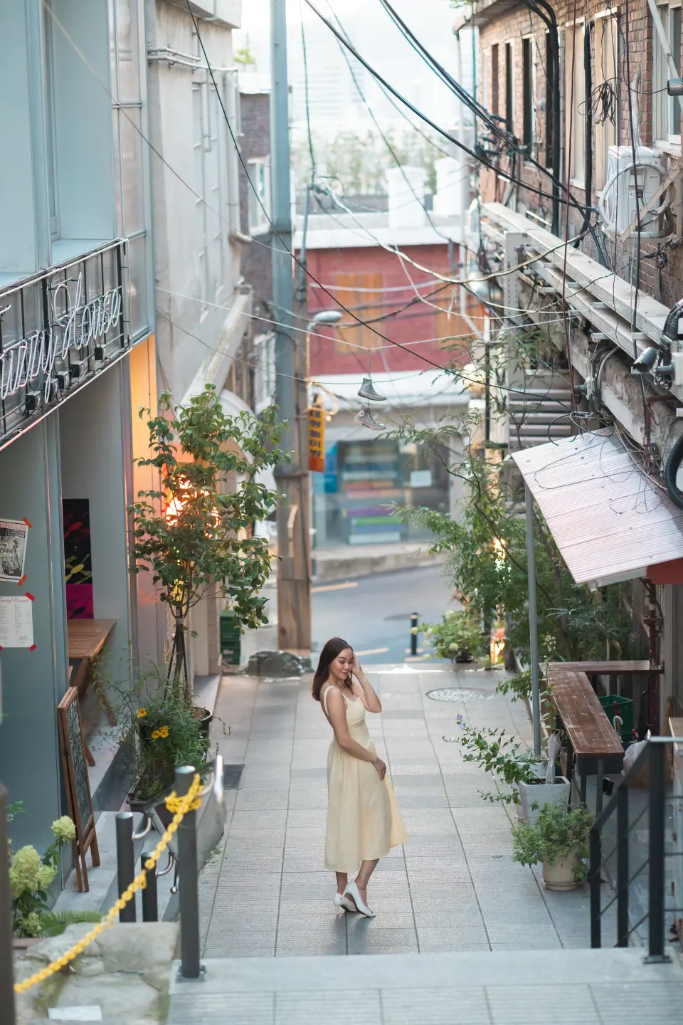A woman in a cream dress walking down an alley lined with shops