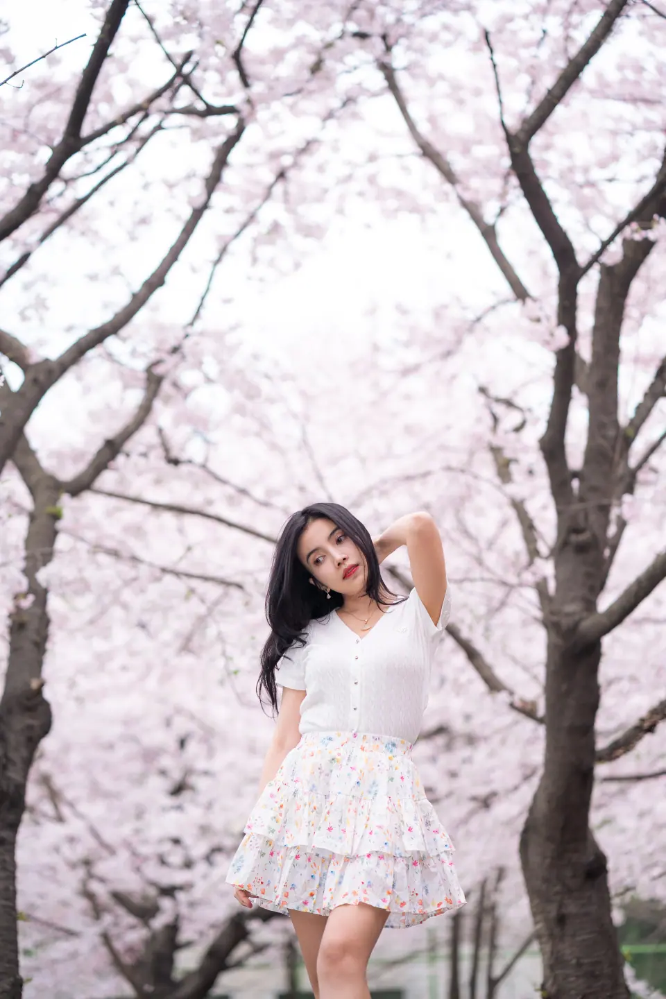 A woman in a white top and ruffled skirt among cherry blossom trees
