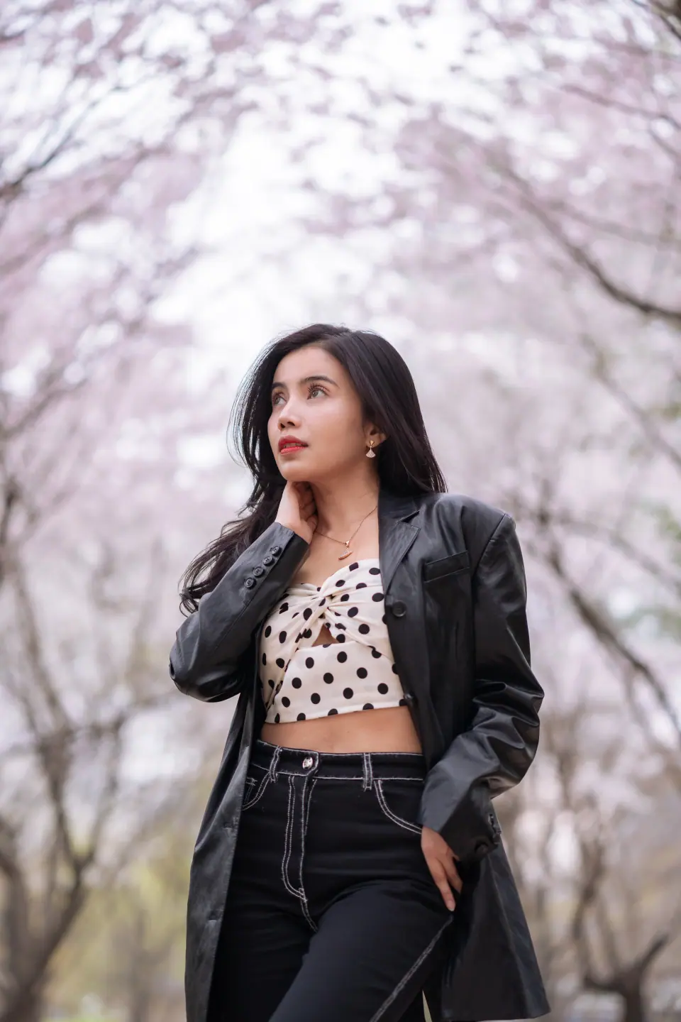 A woman in a leather jacket and polka-dot top under cherry blossoms