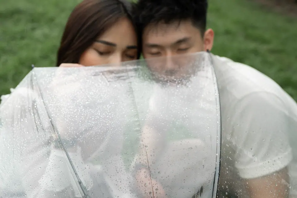 A couple close together behind a rain-speckled umbrella