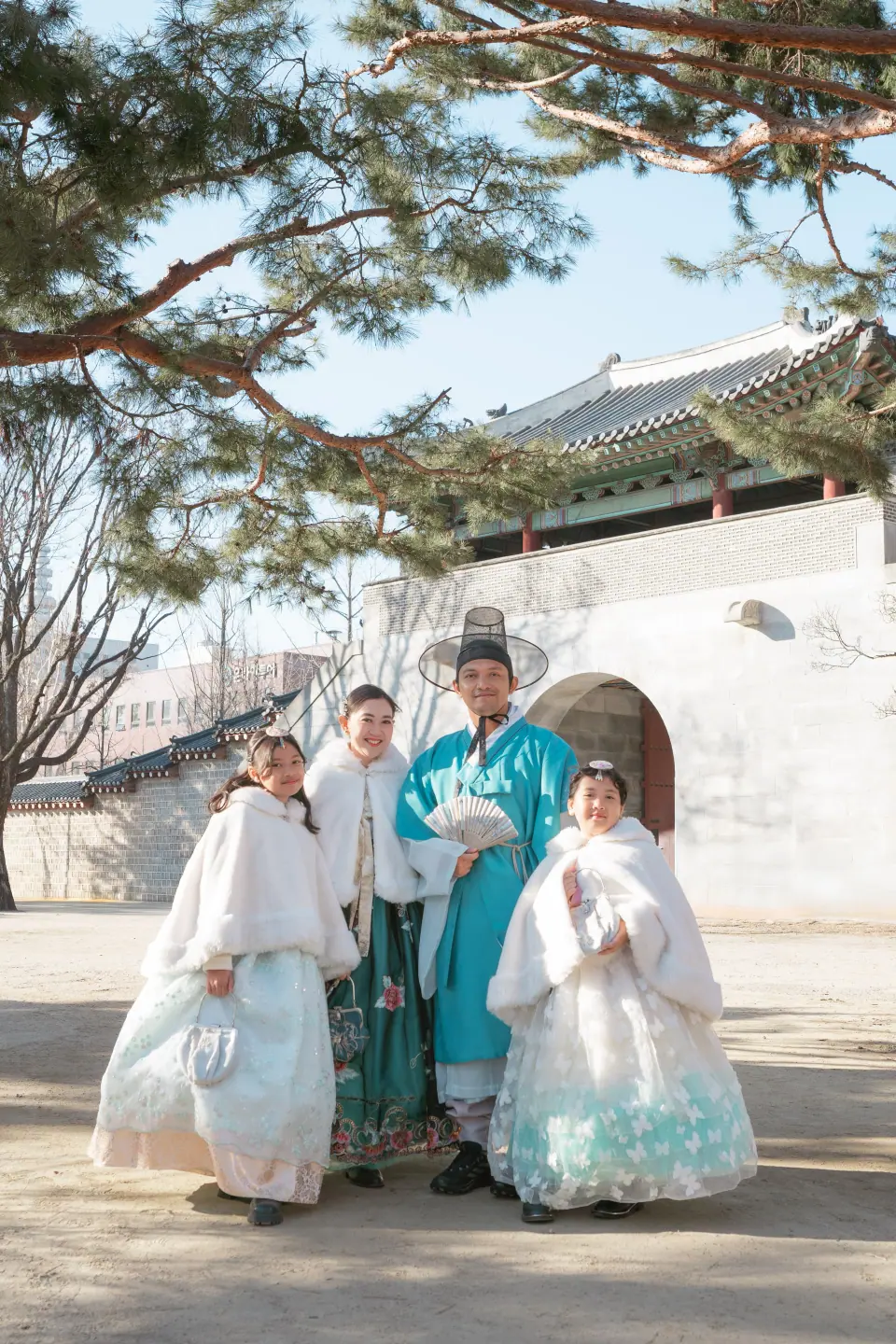 A family in hanbok and white capes at a palace gate