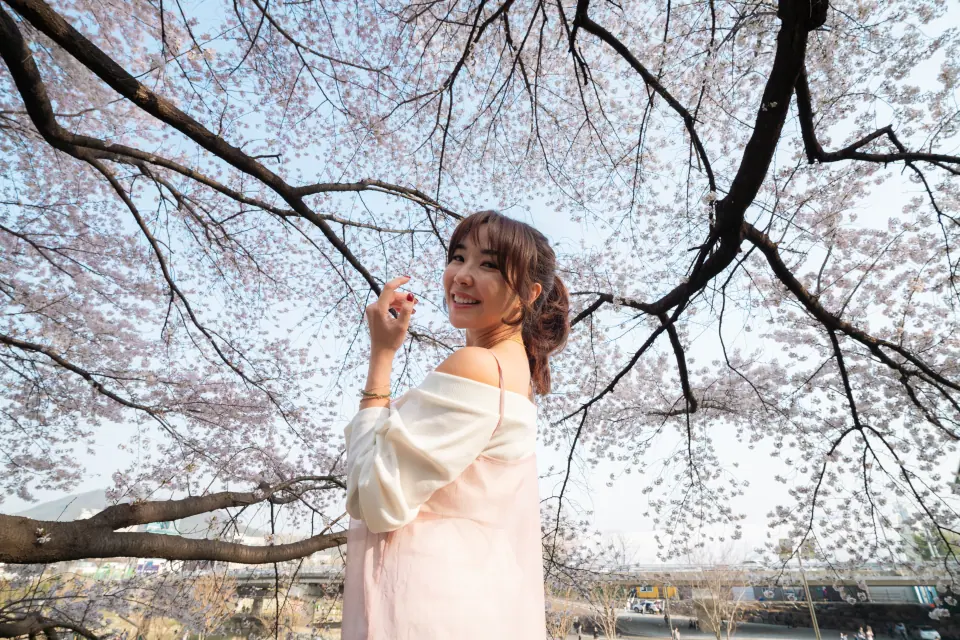 A woman in pink smiling under cherry blossom branches