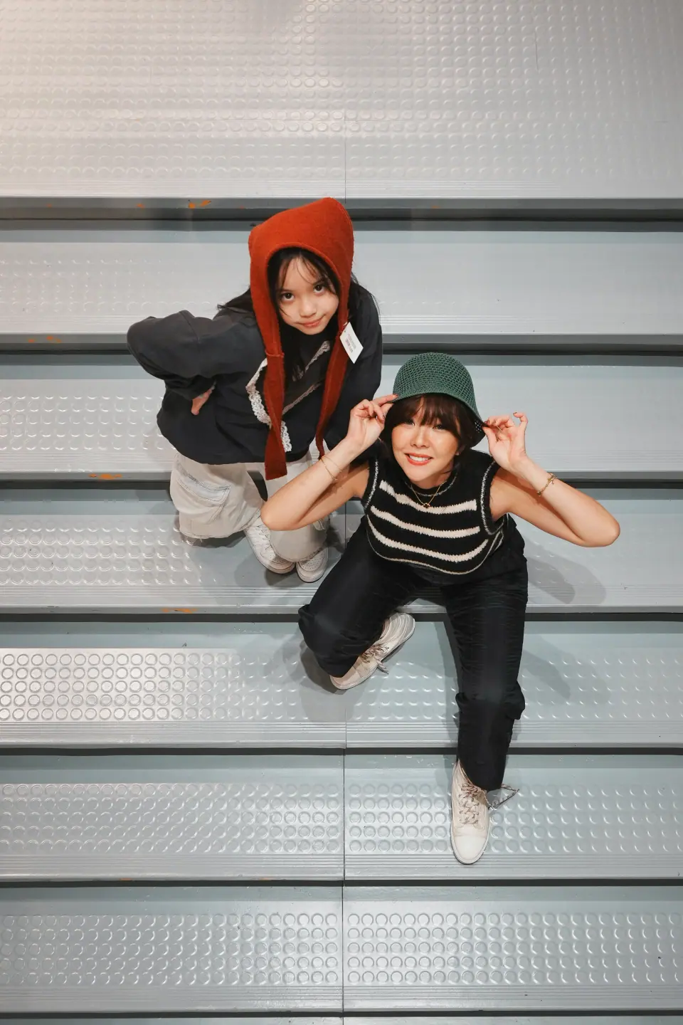 A mother and daughter in knit hats on grey steps