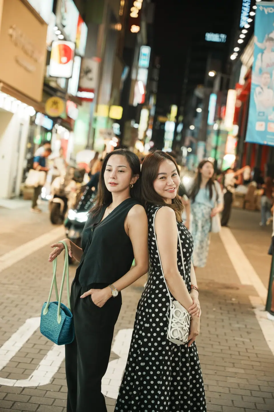 Two friends posing on a busy shopping street at night