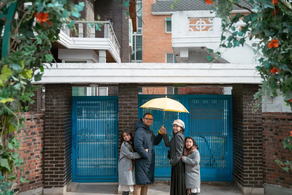 Friends under a yellow umbrella by a blue gate