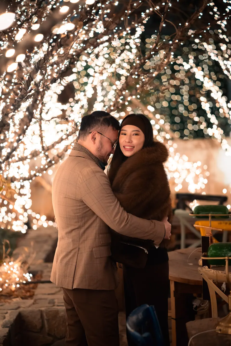 A couple embracing in front of a wall of warm fairy lights