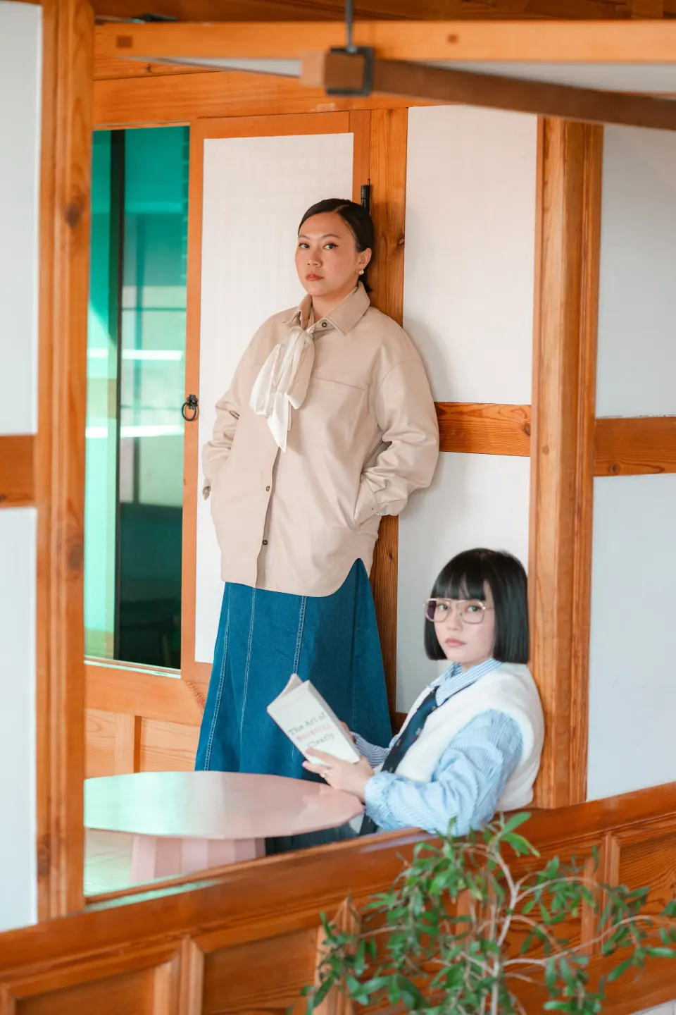Two women in a hanok doorway, one reading