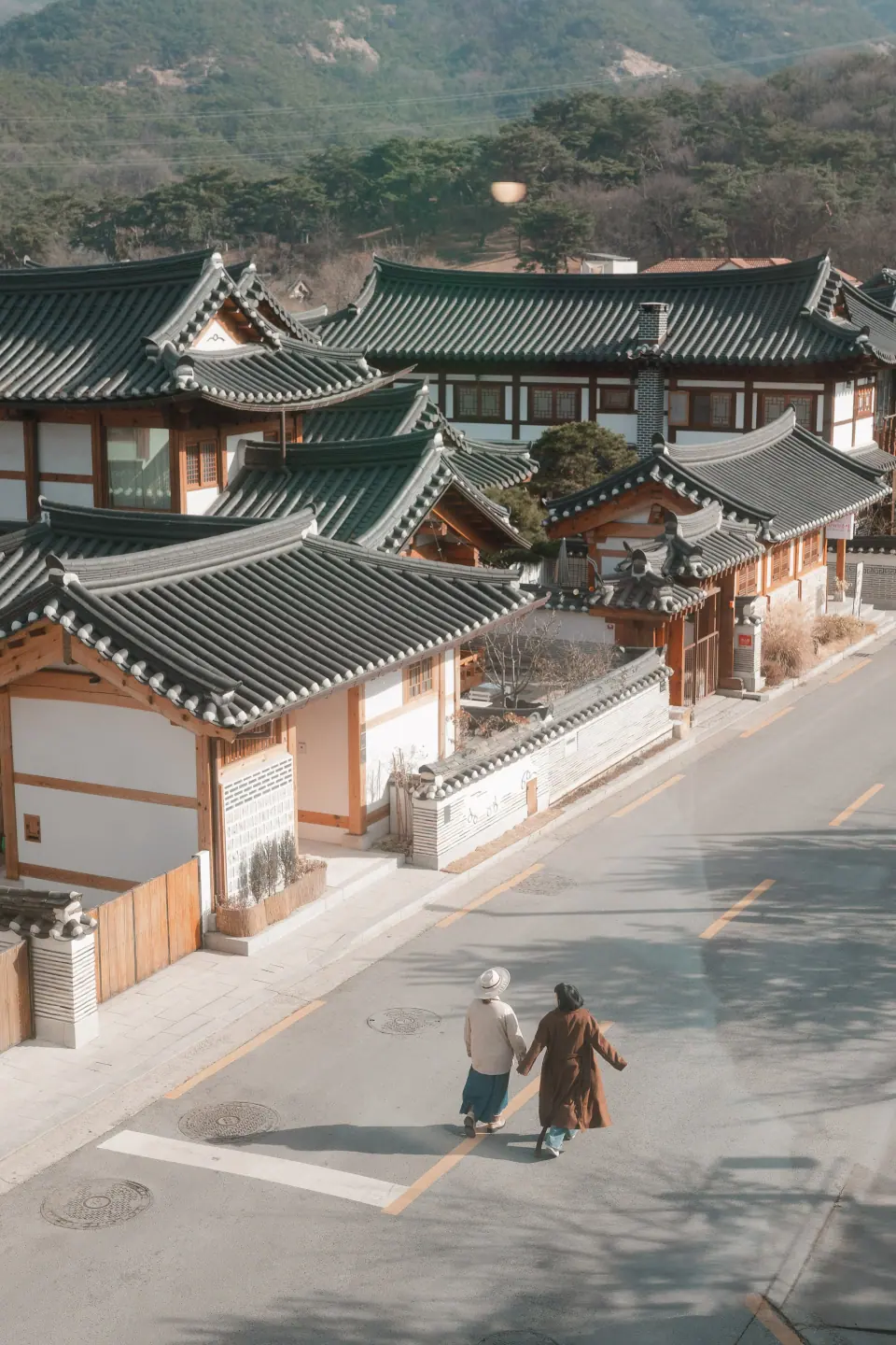 Two people walking through a hanok village, seen from above