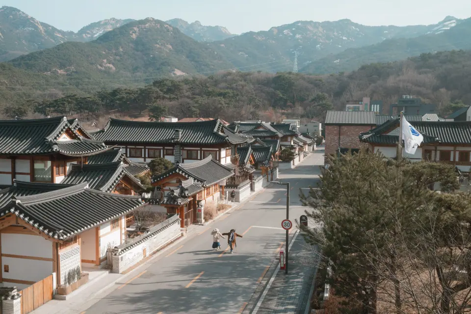 A hanok village beneath the mountains, two people walking the street